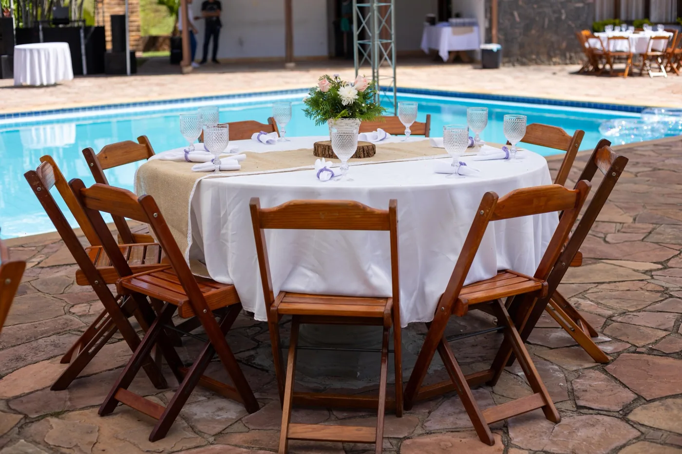 Mesa redonda com cadeiras de madeira em evento próximo à piscina - Nuestra Fiesta Atibaia