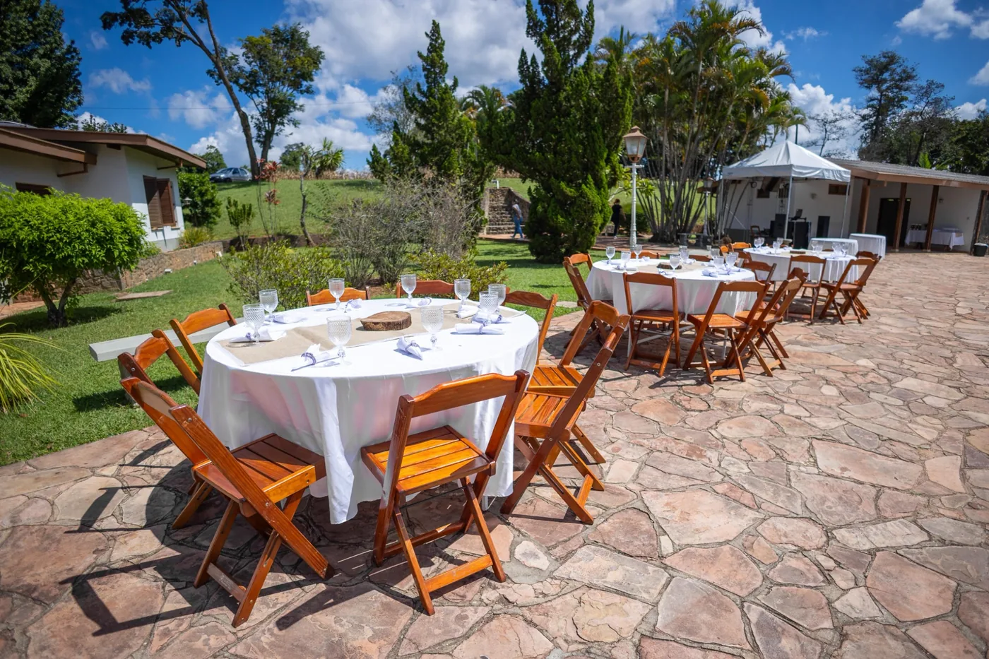 Mesas e cadeiras em área externa com tenda ao fundo - Nuestra Fiesta Atibaia