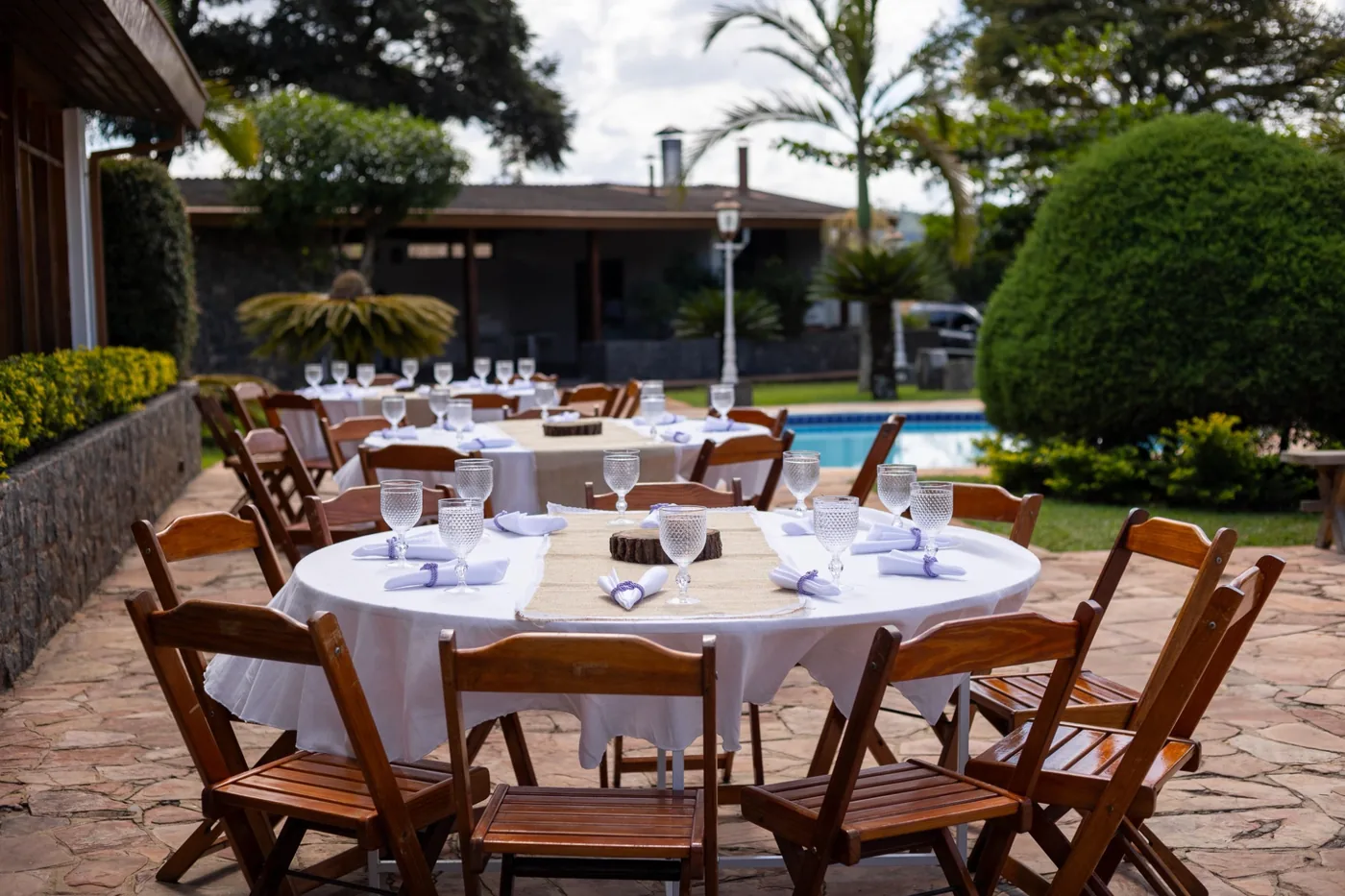 Mesas e cadeiras de madeira montadas em área externa com piscina - Nuestra Fiesta Atibaia